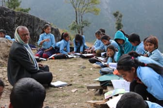 Students studying outdoors in rows on a hillside beside a teacher.